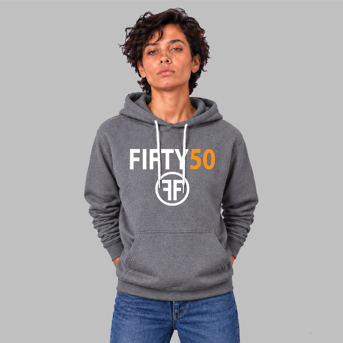 A lady wearing a heather grey hoodie with a logo. The text Fifty is in white bold font and the number fifty is in orange bold font. Under the text are two white Fs, back to back, surrounded by a circle. 