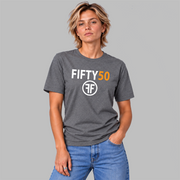 A woman modeling a dark heather gray t-shirt with 'FIFTY50' and a circular 'FF' logo printed on the chest, paired with blue jeans against a solid gray background.