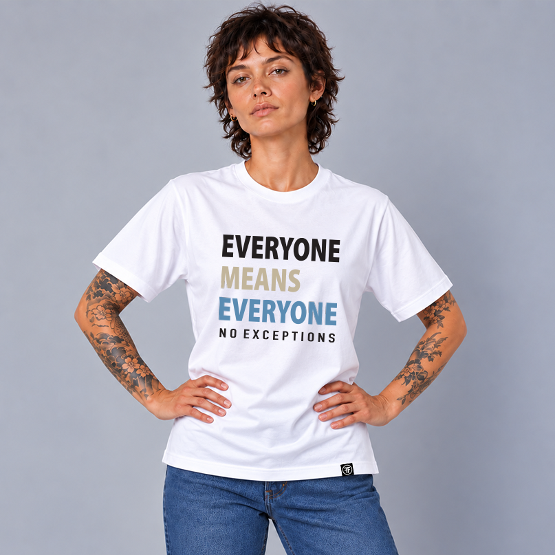 A woman with short dark hair and tattoos wears a white graphic T-shirt with the slogan 'EVERYONE MEANS EVERYONE NO EXCEPTIONS' in black, tan, and slate blue text, paired with blue jeans against a plain gray studio background.