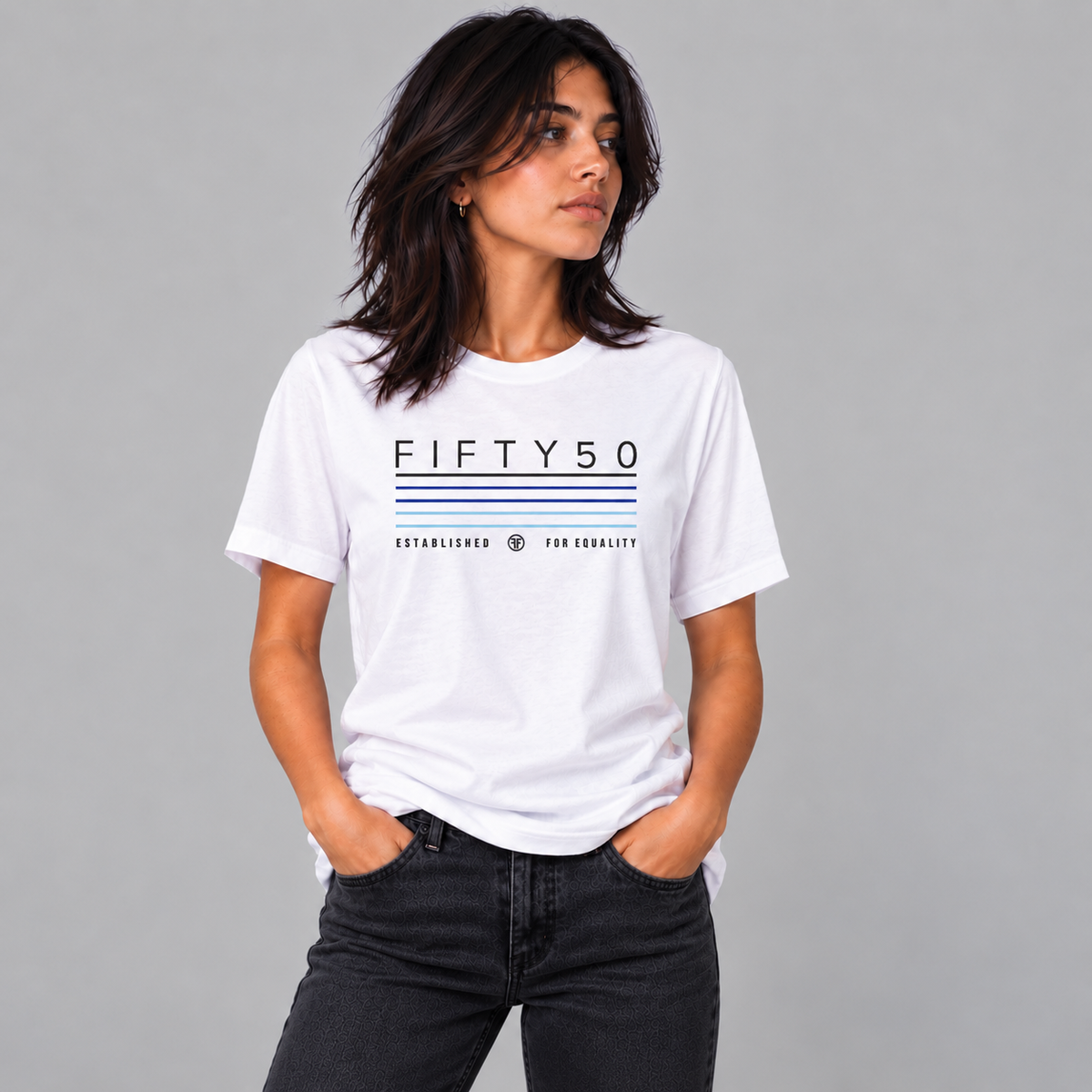 A woman wearing a white short-sleeve graphic T-shirt with 'FIFTY50' and thin black, navy, royal, and light blue stripes printed on the front, paired with light blue jeans, against a plain gray studio background.