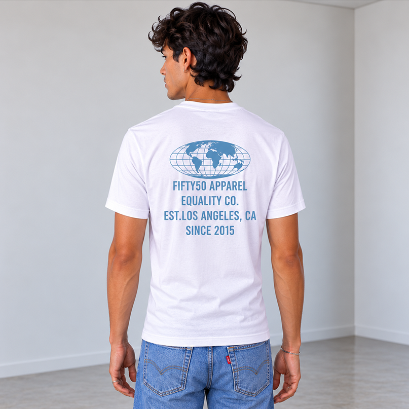 A man viewed from behind wearing a white t-shirt with a Slate Blue graphic print on the back of a globe and the text 'FIFTY50 APPAREL EQUALITY CO, LOS ANGELES, CA, SINCE 2015, paired with blue jeans, against a solid gray studio background.