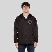 Man wearing a black nylon jacket with black metal buttons. An embroidered patch is sewn on left chest with the text, Fifty50 and Equality below it. Two large Fs are back to back in the center.