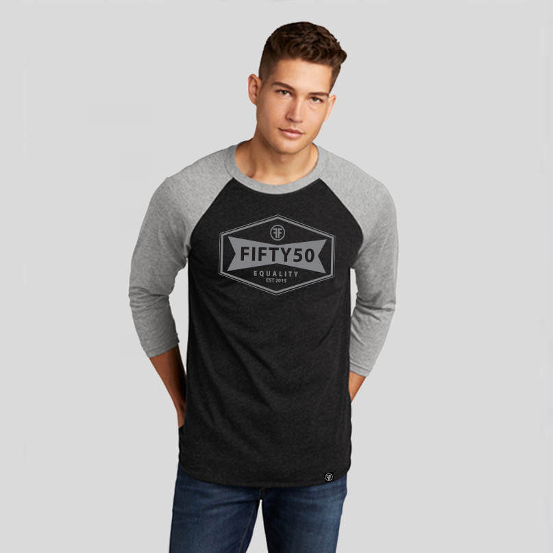 Man wearing a heather black baseball equality tshirt, with a grey collar and arms, and a grey logo. The logo is a narrow, yet wide hexagon with text that says Fifty50, Equality, Established 2015 inside of it.