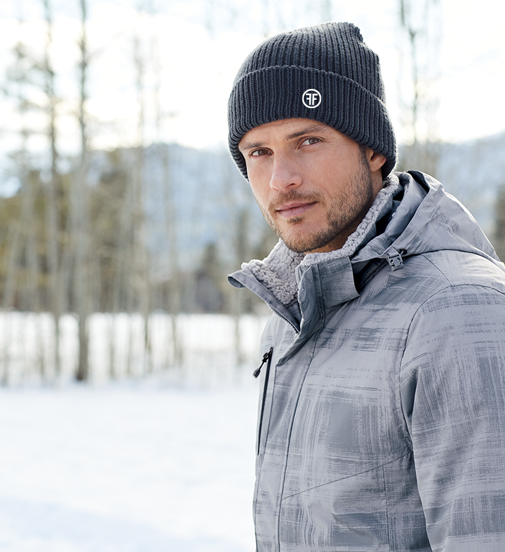 A man wearing a dark grey beanie with a rolled up cuff. It has a white embroidered logo with two Fs, back to back, outlined by a circle, on the left front.